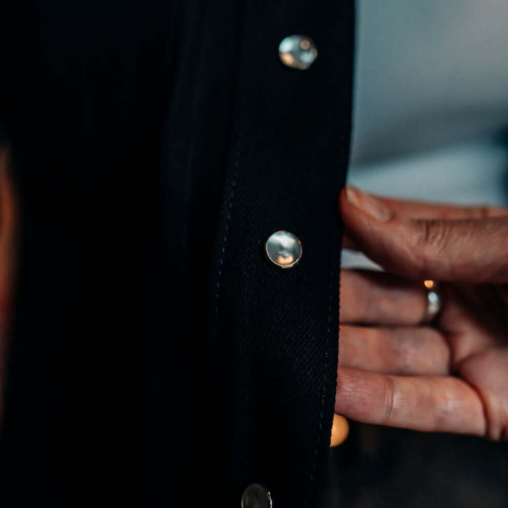 A hand showing the pearl snap detail on a Tobacco Riveter Riding Shirt