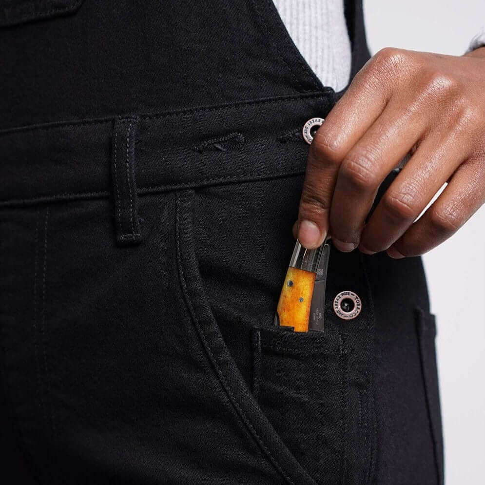 A woman's hand slipping a pocket knife into the side pocket of Boondocks overalls 