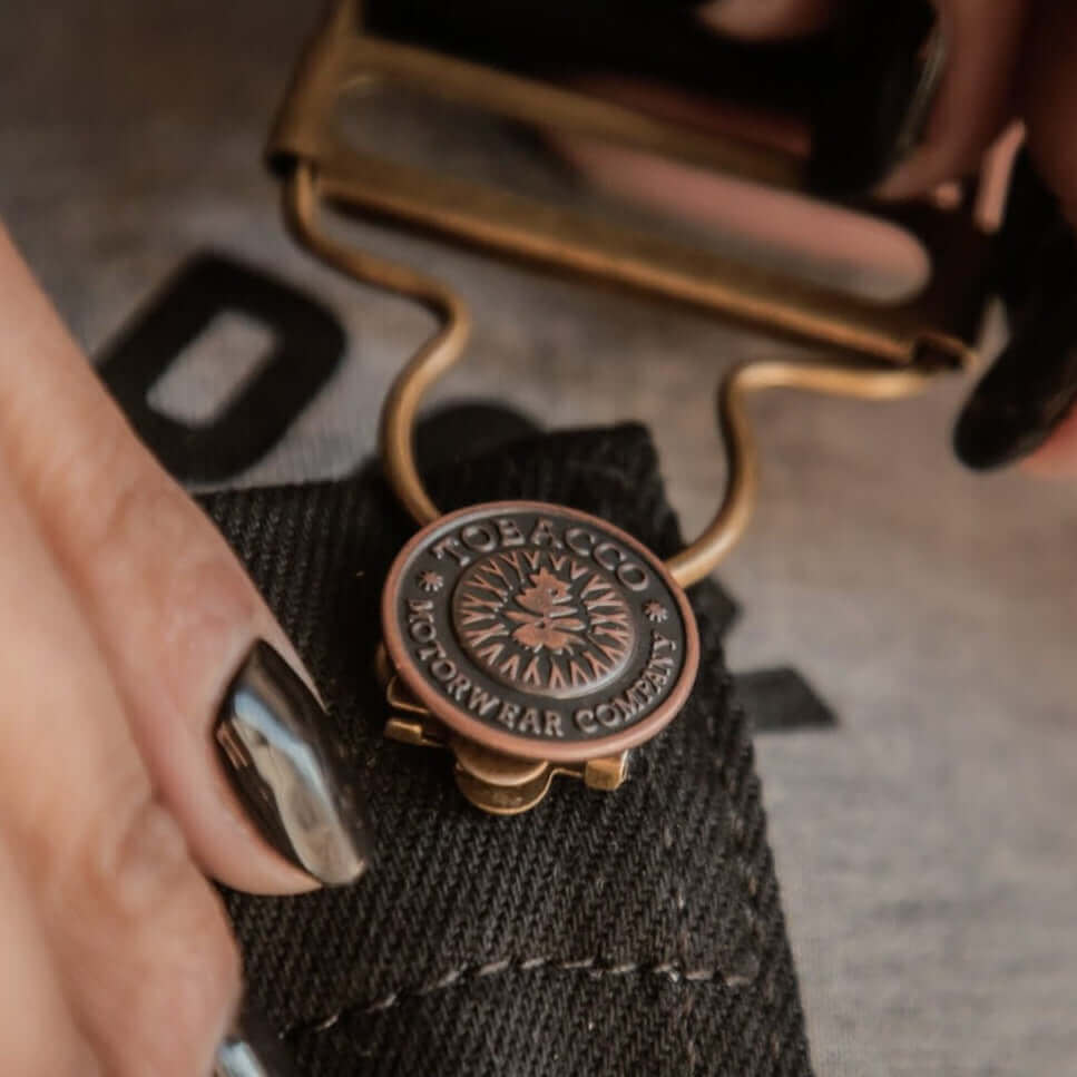 A close up of the metal button and buckle from Tobacco Boondocks riding overalls