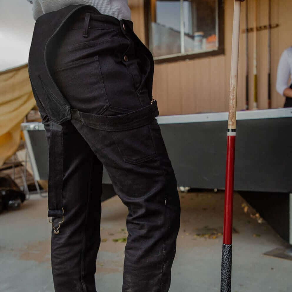 A waist down view of a woman playing pool in Boondocks overalls unbuckled